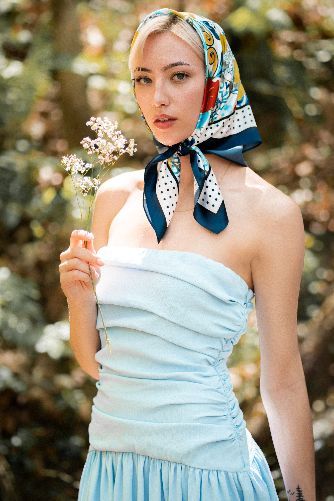 Modelo con pañoleta y top celeste sosteniendo una ramita de flores blancas